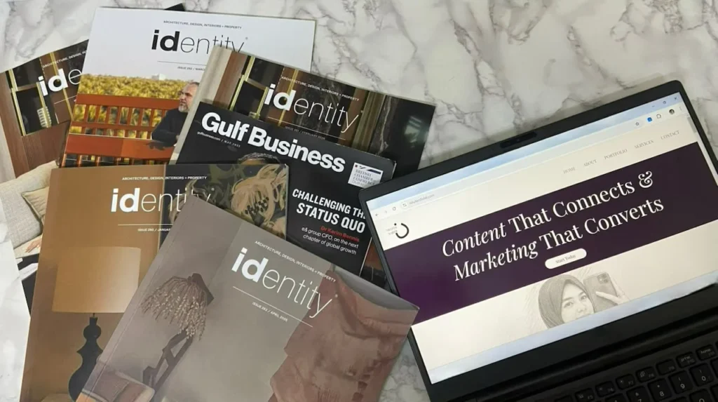 Flat lay of identity and Gulf Business magazines with a laptop portfolio of the best digital marketing strategist in Kochi reading "Content That Connects & Marketing That Converts.